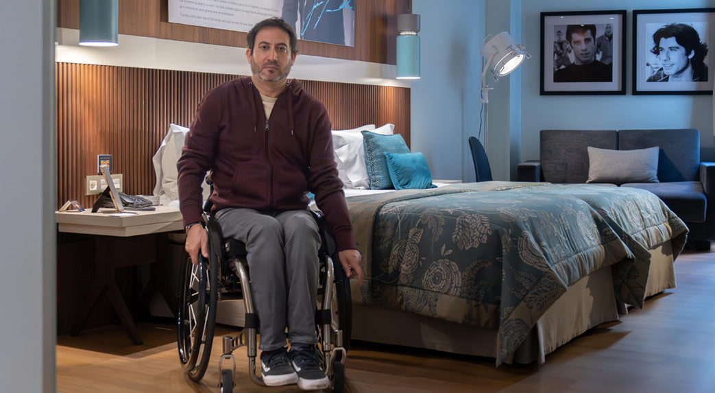 Man in a wheelchair in a well-lit hotel room, with modern and elegant decor.