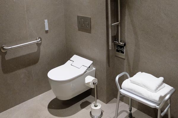 barres d’appui des deux côtés de la cuvette des toilettes adaptées et, à côté, une banquette de douche