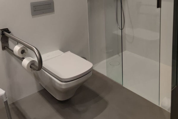 Douche de plain-pied et WC de la salle de bain de la chambre adaptée avec une barre d’appui escamotable. 