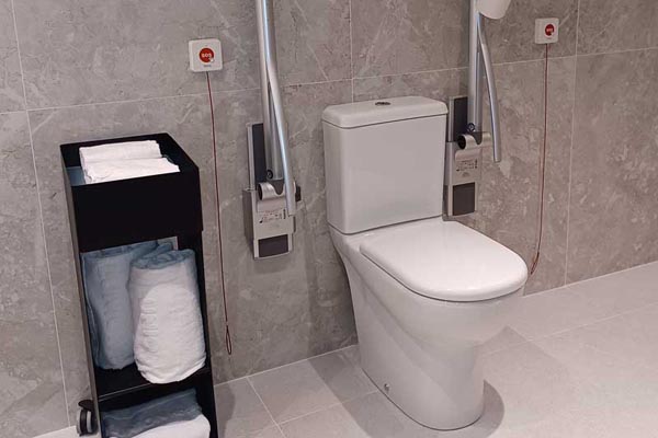 Inodoro del baño de la habitación adaptada con dos barras de apoyo abatibles.