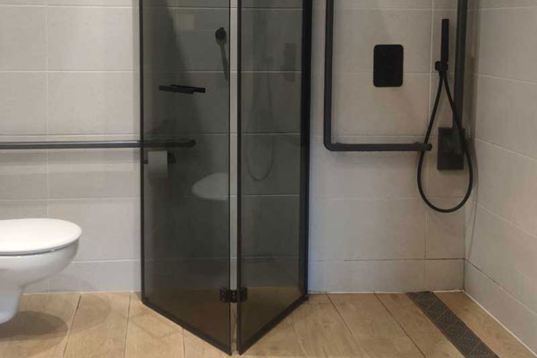 The shower in the adapted room is at ground level and has a fixed L-shaped support bar.