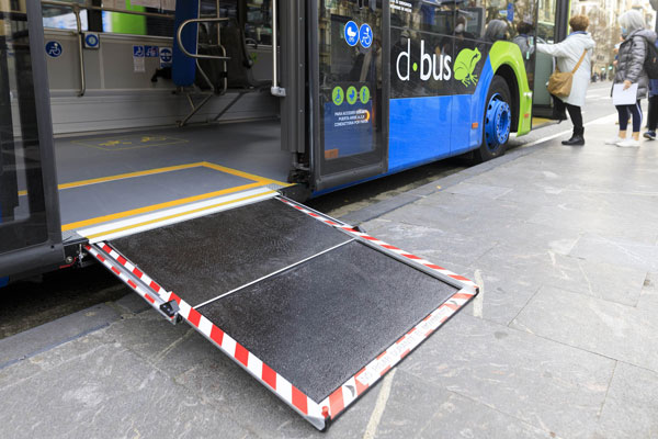 Rampe d’accès de la porte du milieu du bus, entrée signalisée par pictogramme bleu. Rampe déployée et signalisée avec des bandes rouges et blanches aux extrémités.