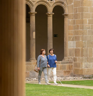 Dos mujeres caminando juntas, una utilizando un bastón para ciegos, en el claustro del Museo San Telmo