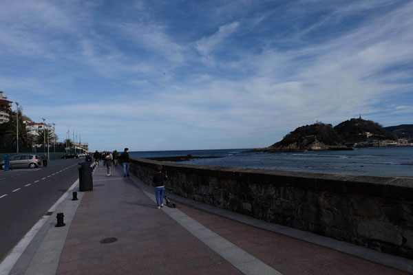 Promenade le long de la plage d'Ondarreta jusqu'au Peine del Viento. Mur de pierre à droite à côté de la mer et route à gauche. 